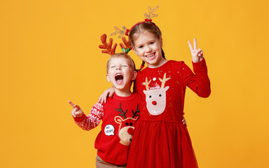 happy funny emotional children boy and  girl in red Christmas reindeer costume  on yellow   background.