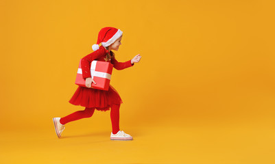 Fototapeta na wymiar happy funny child girl in red running with Christmas gift on yellow background