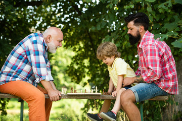 Kid Playing Chess. Handsome grandpa and grandson are playing chess while spending time together outdoor. Happy man family concept playing Chess and have fun together.