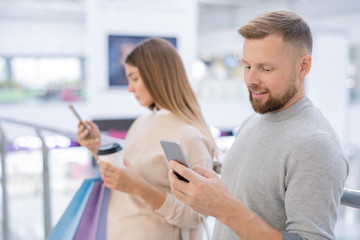 Young man and his girlfriend with smartphones scrolling through online offers