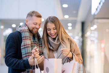 Young shopaholics with paperbags looking at what they purchased on sale