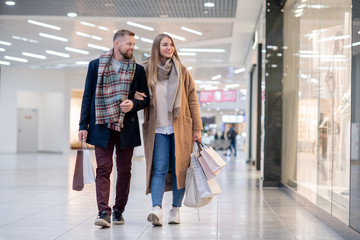 Young casual couple with paperbags looking at clothes in shop window