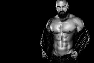 Fototapeta na wymiar Men's fashion concept. Close-up portrait of a brutal bearded man topless in a leather jacket. Athlete bodybuilder on black background.