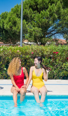 A chinese and a caucasian women sitting on the edge of the pool in affectionate attitude