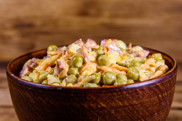 Salad with sausage, green pea, onion and carrot in glass bowl on wooden table