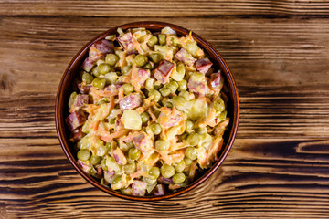 Salad with sausage, green pea, onion and carrot in glass bowl on wooden table. Top view