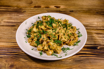 Plate with champignons stewed in sour cream on a wooden table