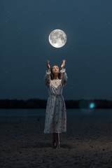 Young attractive girl on the beach stretches her arms to the moon