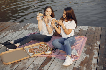 Beautiful girls in a park. Friends sitting near river. Girls eatting pizza