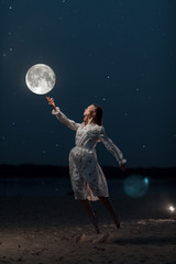 Fototapeta na wymiar Young attractive girl on the beach stretches her arms to the moon