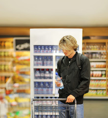 Young men shopping in supermarket, reading product information(water,sparkling water)