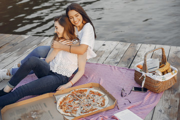 Beautiful girls in a park. Friends sitting near river. Girls eatting pizza