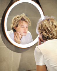 young man looking in the mirror,looking at problems on face
