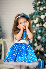 Obraz na płótnie Canvas Cute little girl with a Christmas present, in a blue dress next to decorated Christmas trees. New Year, Christmas family holiday