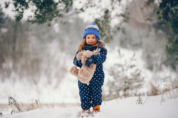 Kid in a winter forest. Girl in a blue hat. Child playing with toy