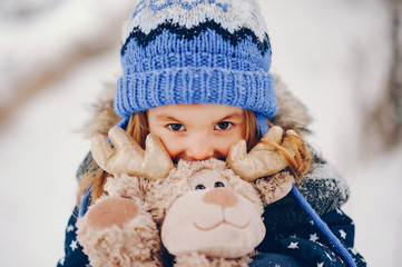 Kid in a winter forest. Girl in a blue hat. Child playing with toy