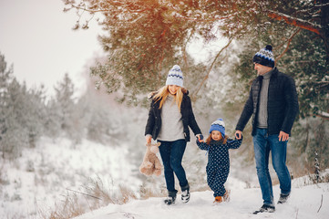 Family have fun in a winter park. Stylish mother in a blue jacket. Little girl in a winter clothes. Father with cute daughter