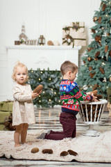 girl and boy playing on the floor with cones to decorate the Christmas tree. brother and sister near the Christmas tree and boxes with Christmas gifts. Merry Christmas and happy holidays