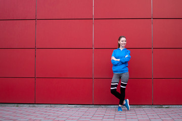 Fototapeta na wymiar sporty girl stands against a red wall in sportswear, fitness woman posing on a city street, copy space