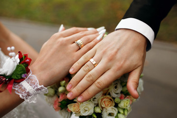Obraz na płótnie Canvas Hands of the newlyweds with rings on their fingers, near a bouquet of roses, the bride and groom hold hands