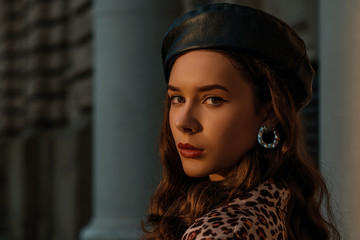 Outdoor close up fashion portrait of young elegant lady wearing trendy faux leather beret, hoop...