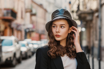 Outdoor close up fashion portrait of young elegant brunette woman wearing faux leather bucket hat,...