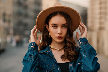 Outdoor close up fashion portrait of young elegant lady wearing beige fedora hat, trendy chain...