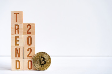 Digits 2020 and the word trend on wooden cubes on a white background next to a bitcoin coin. The...