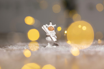 Decorative Christmas-themed figurines. Statuette A little man in a white suit with white skis. Christmas tree decoration. Festive decor, warm bokeh lights.