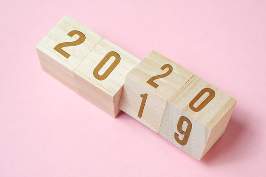 Numbers 2019 change to new year's 2020 on wooden cubes on pink background.