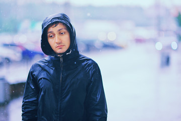 Wet young man with unhappy face walks along the street during heavy rain, close-up