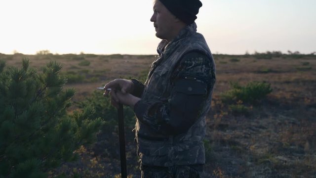 hunter hides behind a cedar bush smokes