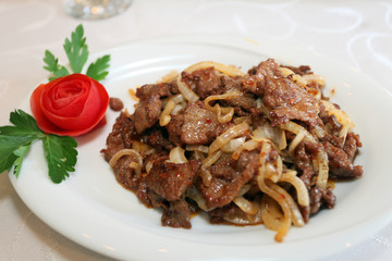 Meat meal with onion and red rose on the dinner plate