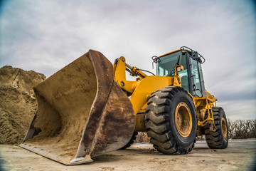 Side view of a yellow bulldozer with dirty metal bucket and black rubber wheels