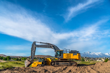 Excavator at a construction site with mountain homes and cloudy sky background