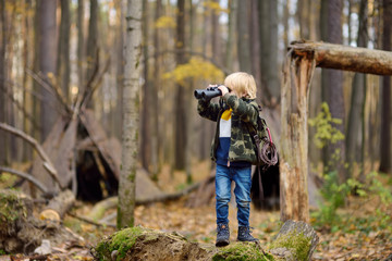 Little boy scout with binoculars during hiking in autumn forest. Child is looking through a...