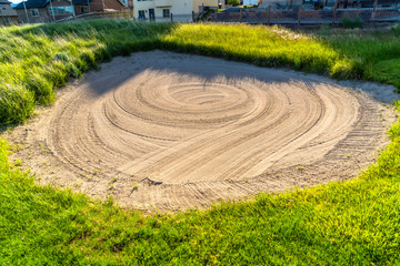 Close up of a sand trap surrounded by grasses at a golf course on a sunny day