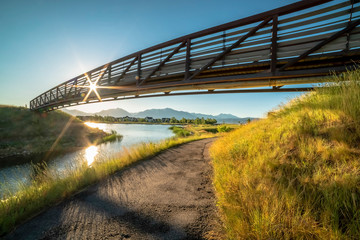 Trail along a lake and passing under a bridge with sun and blue sky overhead