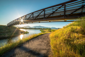 Fototapeta premium Trail along a lake and passing under a bridge with sun and blue sky overhead