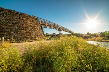 Bright sun and blue sky over a lake and bridge with view of homes and mountain