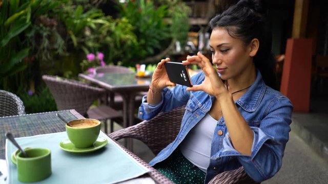 Young woman taking photo of coffee with cellphone in cafe