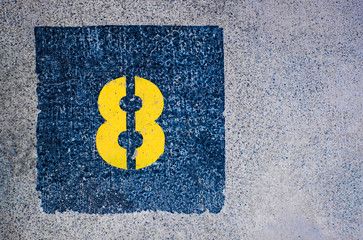 Yellow number 8, eight, in dark blue square, offset on flat concrete surface.