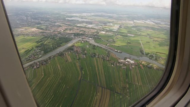 Window seat view of an airplane flying over Rotterdam, The Netherlands on a cloudy summer day.