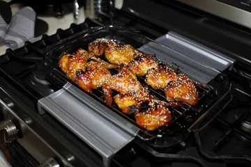 Baked teriayki chicken wings from the oven resting on the stove top in a home kitchen.