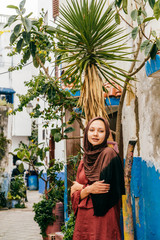 Muslim woman stands by the wall in the blue city of Morocco in a headscarf