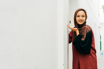 Fototapeta na wymiar Muslim woman stands by the wall in a scarf and smiles