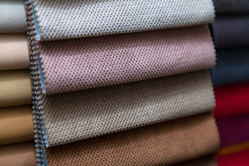 Pieces of textile material for interior trim and furniture making for example in the catalog of different colors for the design studio. Many colored materials hanging on the wall in stock.