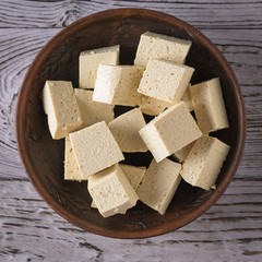 Pieces of tofu cheese in a clay plate on a wooden background. Soy cheese. Flat lay.
