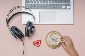 Hand with a Cup of coffee, a laptop and headphones on a coral background. Job.