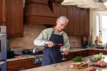 Handsome senior man in the kitchen pouring wine